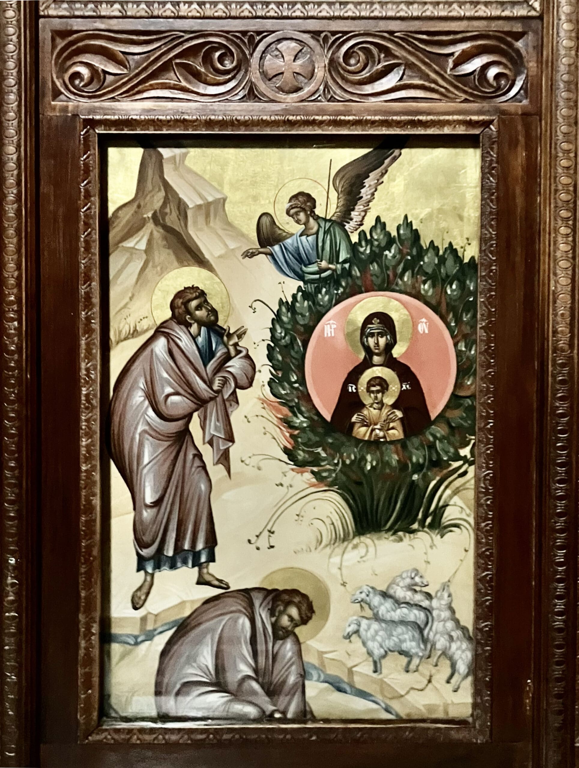 Religious icon depicting Moses before the burning bush, with an angel above and the Virgin Mary holding baby Jesus within the bush. Sheep graze nearby, all set in an ornate wooden frame.