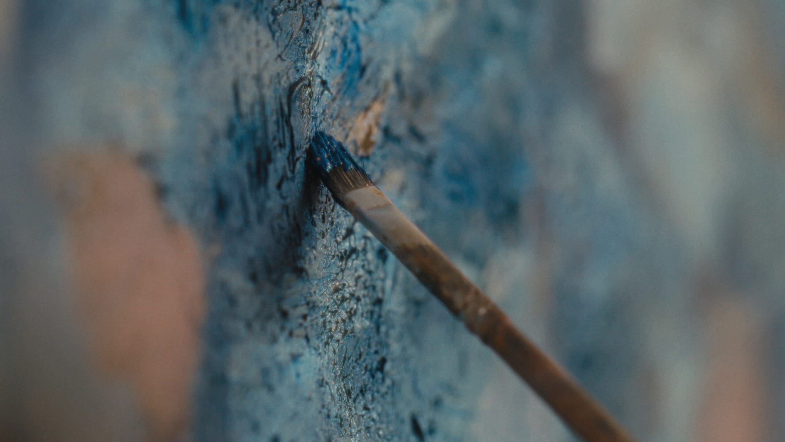 A close-up of a paintbrush applying blue paint to a textured surface, capturing fine details of the brush bristles and paint strokes.