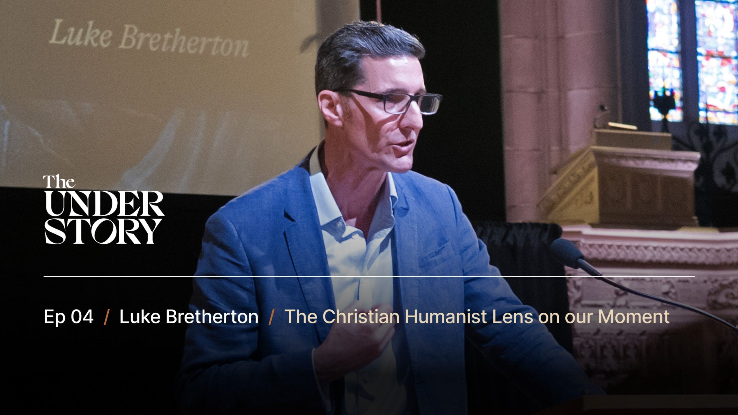 A man in a blue suit and glasses speaks at a podium in a church. Text reads: The Understory. Ep 04 / Luke Bretherton / The Christian Humanist Lens on our Moment. A screen and stained glass window are visible behind him.